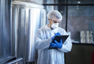 Concentrated technologist expert in white suit controlling production in food factory.